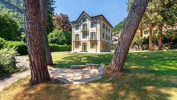 A multi-story building with a symmetrical facade, a central entrance, and a surrounding grassy area with trees.