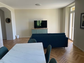 Ein Wohnzimmer mit Fernseher auf einem Schrank, einer Couch, einem Esstisch und einem hellblauen Korpus.