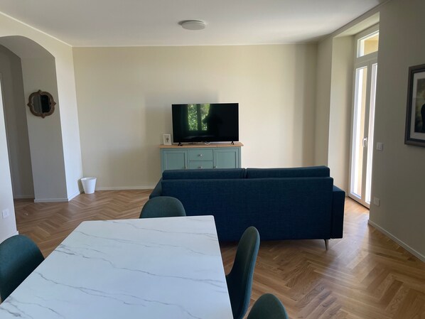 A living room with a TV on a stand, a sofa, a dining table, and a light blue cabinet.