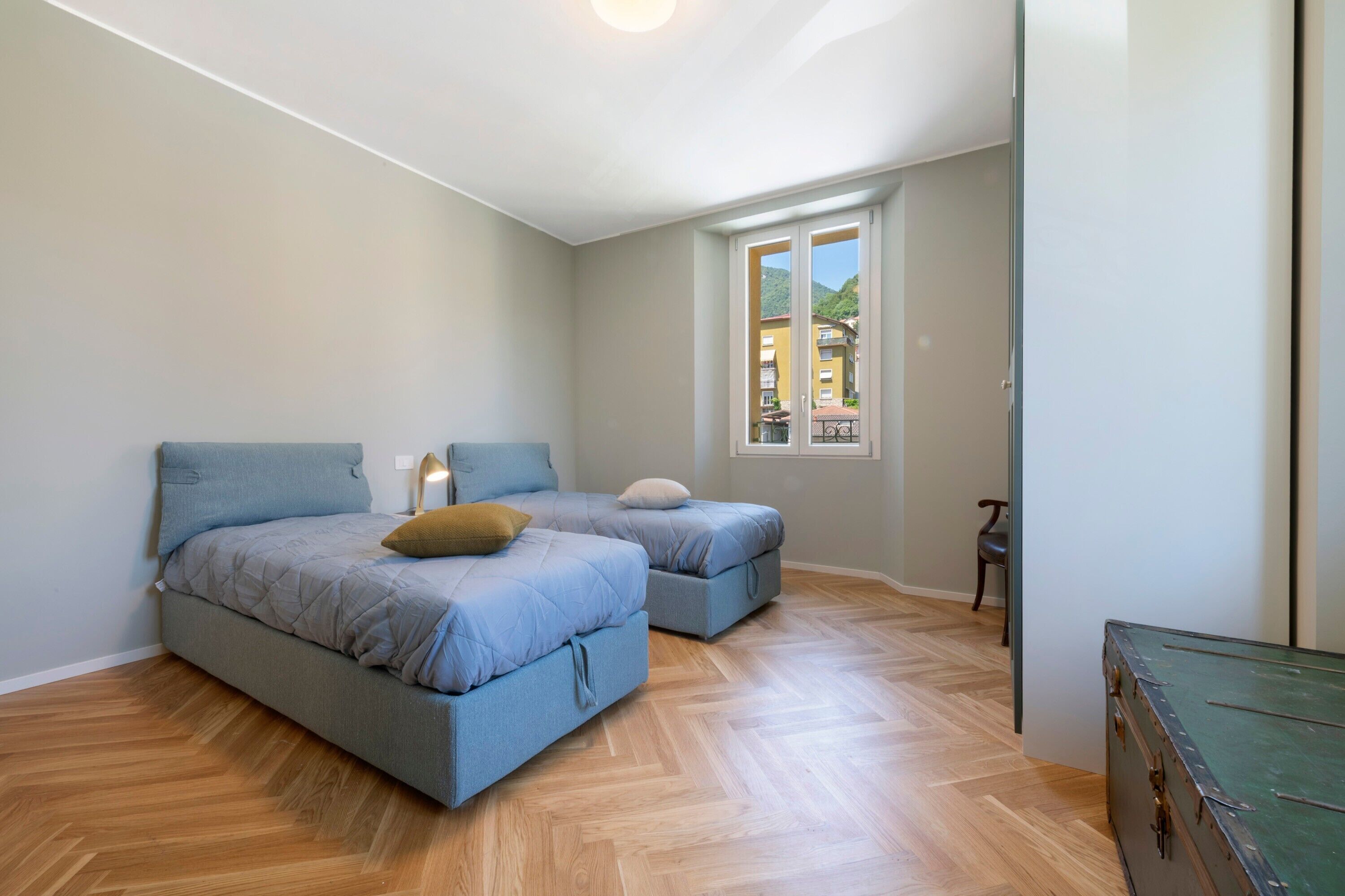 Quarto com duas camas, janela com vista para edifícios e piso de madeira.