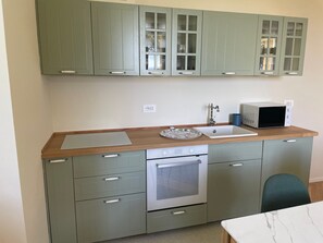 A kitchen with green cabinets, a microwave, a sink, and a wooden countertop.