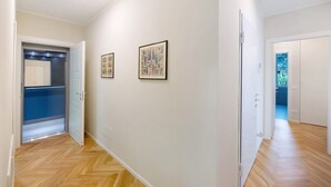 Un pasillo con piso de madera, paredes blancas y cuadros enmarcados.