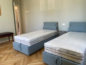 A room with two single beds, a bench, a small round table, and a door leading to another room.