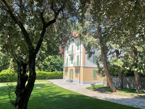 A building with a stone pathway leading to a gated entrance, surrounded by lush greenery and trees.