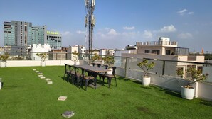 A rooftop terrace with a dining table and chairs, potted plants, and a view of surrounding buildings. - Hotel Rove Inn (Indore)