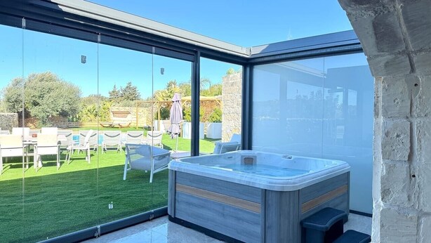 Uma área moderna com hidromassagem ao ar livre, cercada por vidro, gramado e móveis de exterior.