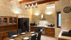 Cozinha com paredes de pedra, mesa de jantar posta para quatro pessoas, frigorífico, micro-ondas e pia.