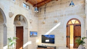 Uma sala de estar ampla com paredes de pedra, vigas de madeira, uma televisão grande e assentos confortáveis.