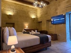 Ein Hotelzimmer mit Steinkamin, einem Bett mit Kissen, einem Nachttisch mit Lampe und einem an der Wand befestigten Fernseher.
