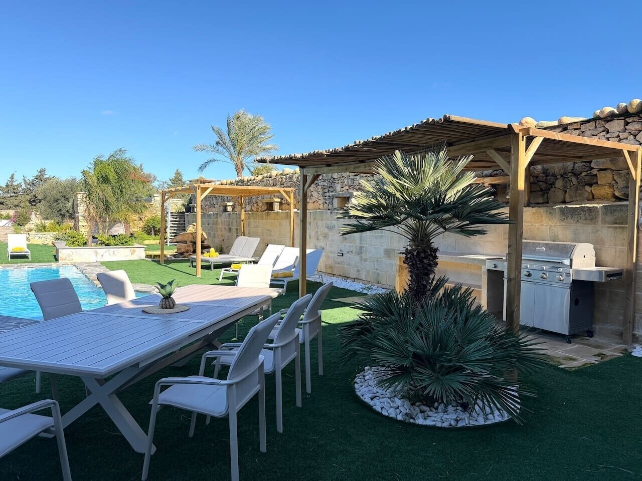 A poolside area with a table and chairs, a grill, and a covered seating area.