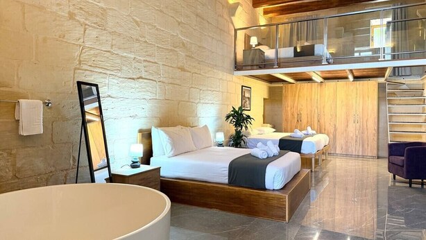 Hotelkamer met een groot bed, een tweede bed, een balkon, een trap en een badkamer met een ruime badkuip.