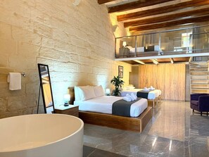 A hotel room with a large bed, a second bed, a balcony, a staircase, and a bathroom with a large tub. - Girgor Farmhouse W/Pool&Jacuz byArcoCollection (St. Paul`s Bay)