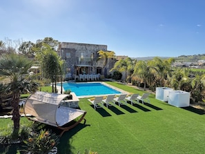 Ein Swimmingpool mit Liegestühlen, einer überdachten Sitzecke und einem Steinhaus im Hintergrund.