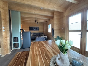 A wooden interior with a dining table, a sofa, a fireplace, and a window. - Modern log cabin with sauna, natural views, and chalet charm (Lisberg)
