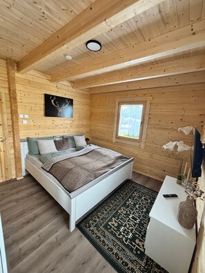 Ein Schlafzimmer einer Holzhütte mit einem Bett, einem kleinen Tisch, einem Fenster und einer Deckenleuchte.