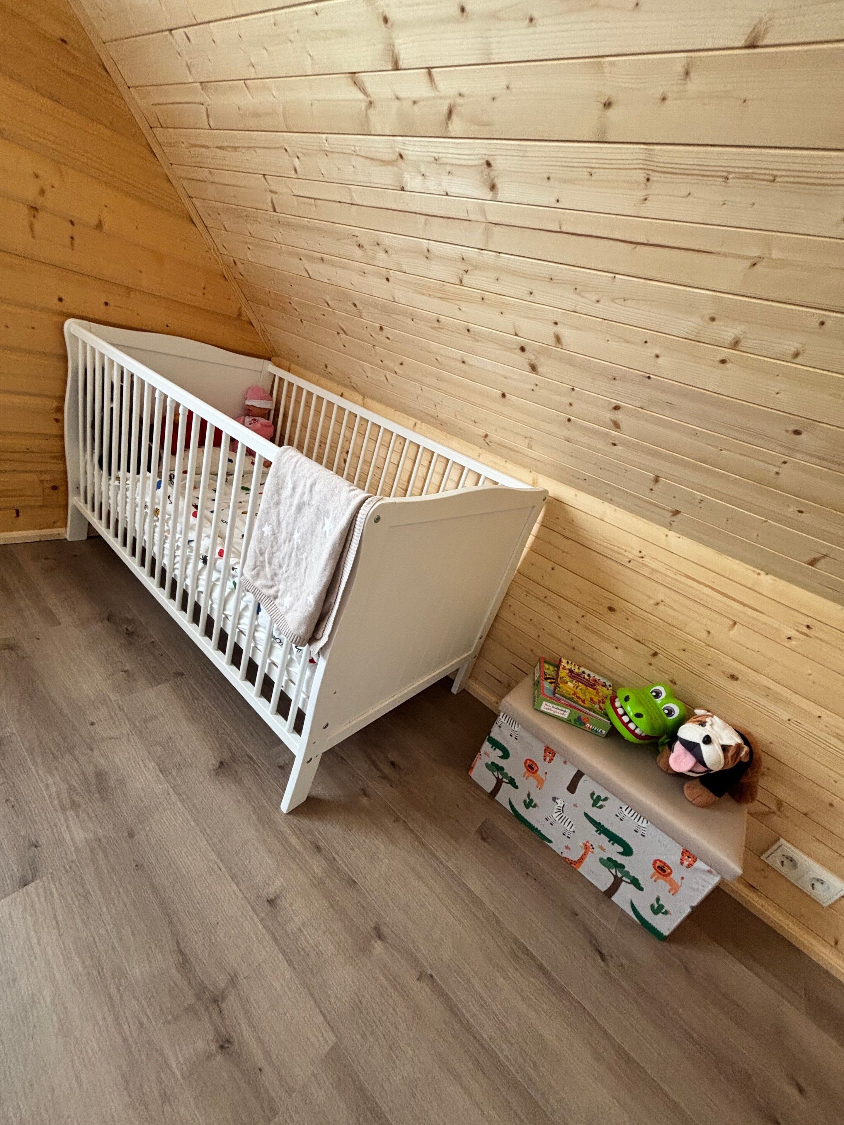 A wooden crib in a room with a sloped ceiling and a wooden floor.