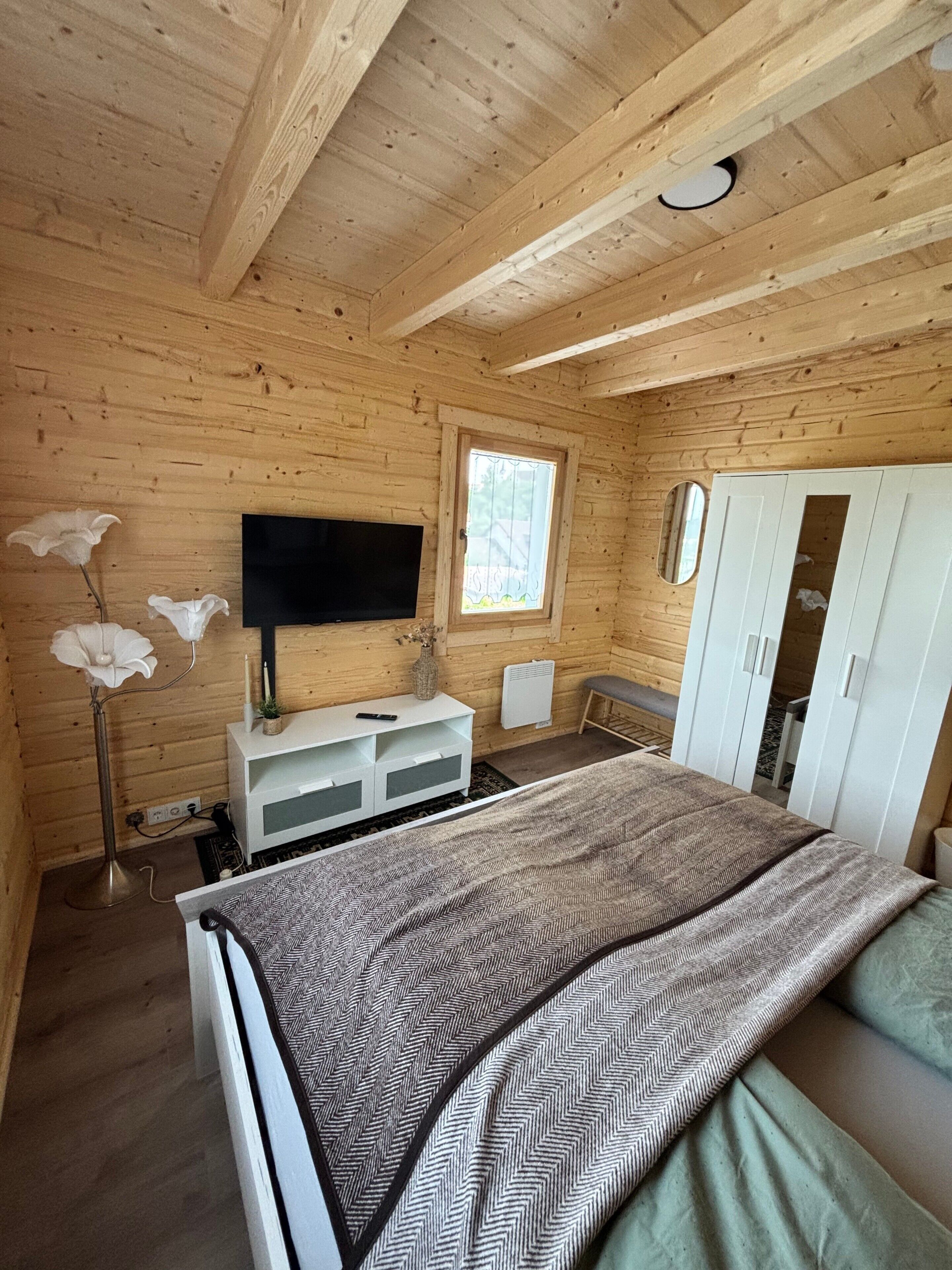 A wooden cabin room with a bed, a TV, a wardrobe, and a window.