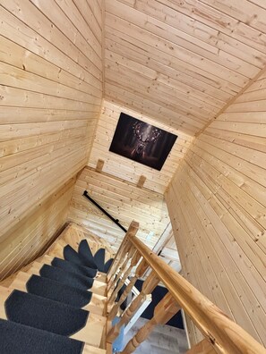 A wooden interior with a staircase, a window with a dark frame, and a wooden railing.