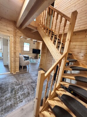 A wooden staircase with a handrail leading to an upper level. A flat-screen TV is mounted on the wall in the background. - Modern log cabin with sauna, natural views, and chalet charm (Lisberg)