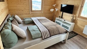 A wooden cabin bedroom with a bed, pillows, a TV, and a window.