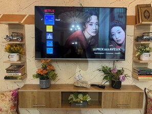 Ein an der Wand befestigter Fernseher zeigt eine Netflix-Oberfläche mit dem Titel 'LE PRIX DES AVEUX' und Optionen für 'Psychologisch', 'Spannungsgeladen' und 'Mysteriös'.