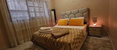 A hotel room with a bed, a nightstand, a lamp, and a window with curtains.