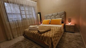 Une chambre d’hôtel avec un lit, une table de chevet, une lampe et une fenêtre avec des rideaux.