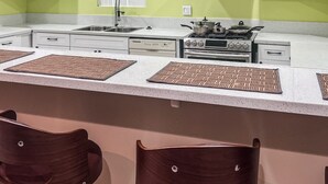 A modern kitchen with white cabinets, a stainless steel sink, and a gas stove. There are two bar stools with dark seats. - @ View Suite with private entrance, Lounge and sofa bed and bar. (Los Angeles)