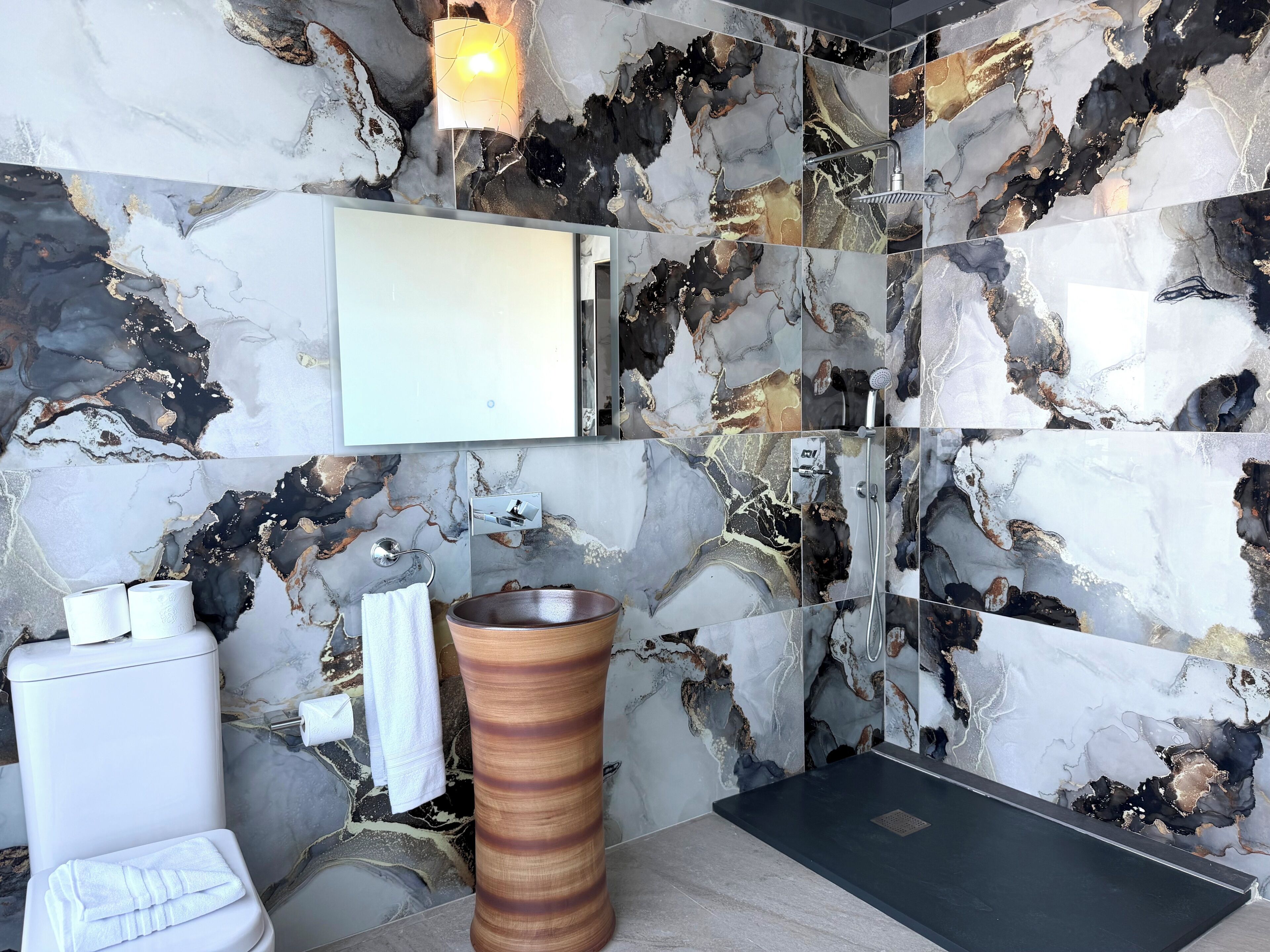 A bathroom with a marble backsplash, a wooden vessel sink, a toilet, and a shower area.