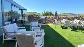 A modern outdoor patio with white furniture, a stone wall, and a clear view of the surrounding landscape.