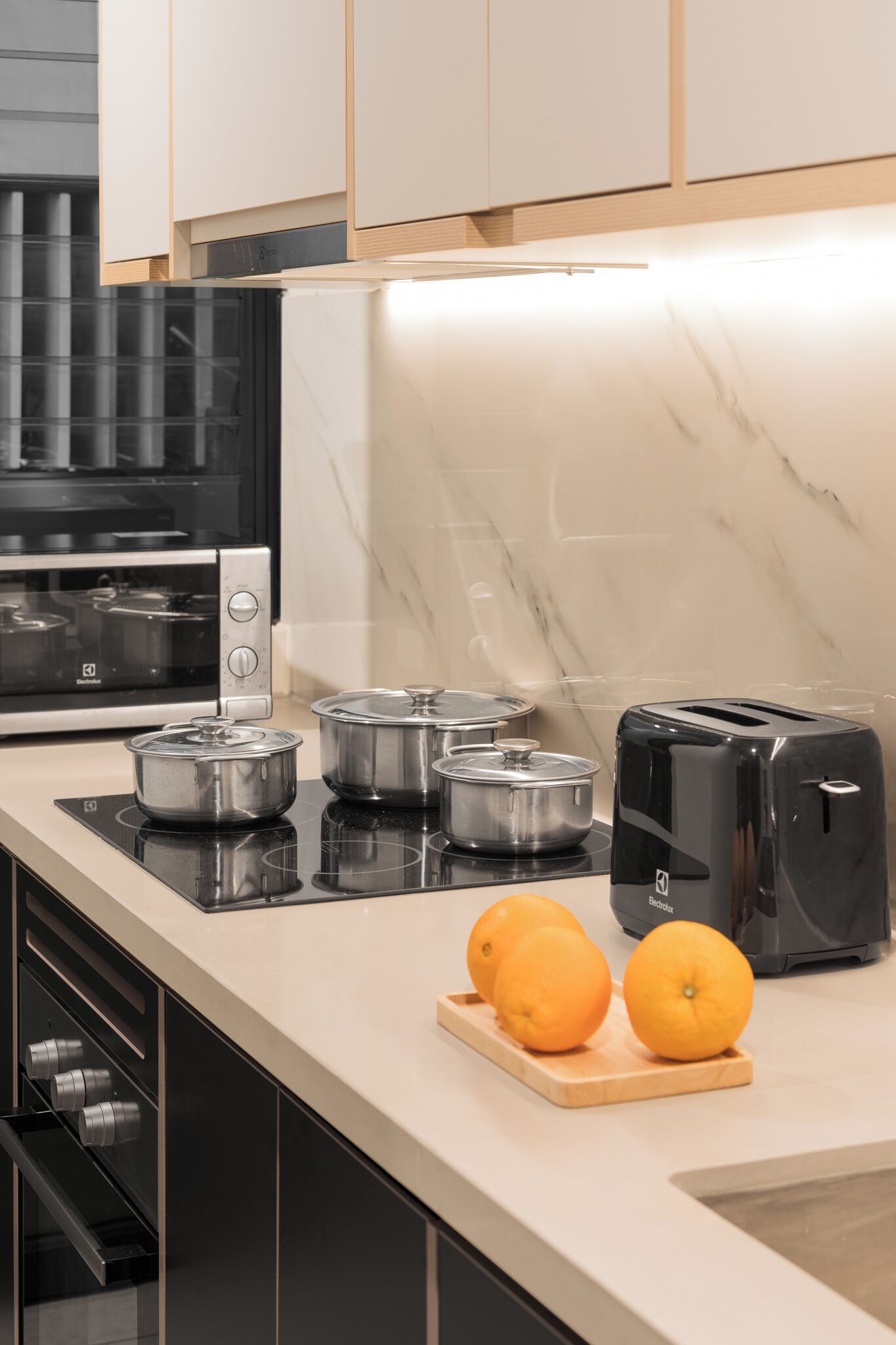 Una cocina moderna con horno empotrado, tostadora y encimera con dos naranjas.