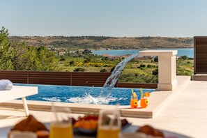 A pool with a waterfall feature, a view of a lake, and a distant landscape. - Villa Ana Zadarvillas (Razanac)