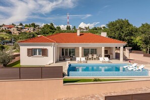 Ein modernes Haus mit Swimmingpool, einer Terrasse mit Liegestühlen und Blick auf die umliegende Nachbarschaft.
