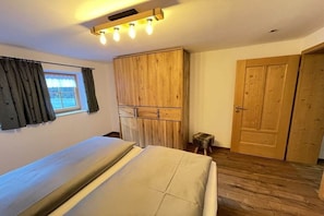 Ein Schlafzimmer mit einem Bett, einem Holzschrank, einem kleinen Hocker und einer Tür.
