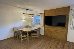 Ein Essbereich mit Holztisch und -stühlen, einer Bank, einem an einer Holzwand montierten Fernseher und einem Fenster mit Vorhängen.