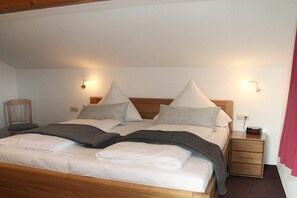 A neatly made bed with pillows, a bedside table with a clock, and a wall-mounted light fixture. - Basement - Lake view (Hopfen am See)