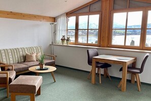 A cozy room with a sofa, a small table, a chair, and a window with a view of a lake and mountains. - Basement - Lake view (Hopfen am See)