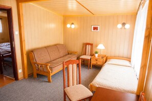 Ein Zimmer mit Holzbalkendecke, einem Bett, einem Sofa, einem Sessel, einem kleinen Tisch und Wandleuchten.