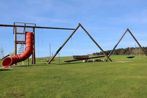 Ein Spielplatz mit einer roten Rutsche, Schaukeln und einer Kletterkonstruktion.