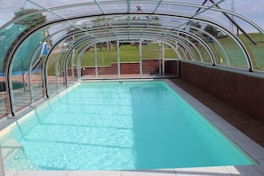 Ein Pool mit Glasumrandung, umgeben von einer Ziegelwand und einer Rasenfläche.