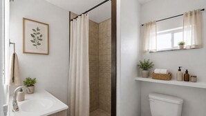Et badeværelse med bruser, toilet, vask og en planteskjuler på væggen.