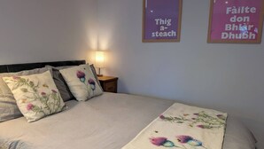 A bedroom with a bed, pillows, a nightstand, and two framed signs on the wall. - The Highland Studio - Nc500's Home From Home (Muir of Ord)