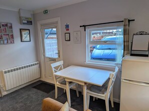 Ein Zimmer mit einem weißen Tisch, Stühlen, einem Heizkörper, einem Fenster mit Blick auf ein Auto und einer Tür mit einem Brandschutzschild.