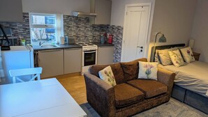 A compact living space with a kitchenette, a sofa, a bed, and a dining area. - The Highland Studio - Nc500's Home From Home (Muir of Ord)