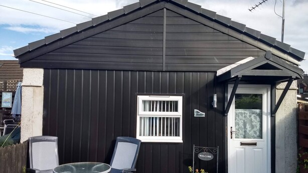 A small black metal shed with a white door, a window, and a welcome sign. - The Highland Studio - Nc500's Home From Home (Muir of Ord)