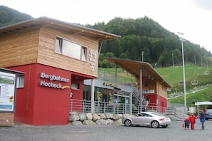 Ein Gebäude mit roter Holzfassade, einer Beschilderung für 'Bergbahnen Hocheck' und einem Schild mit 'Sport Brosig'.