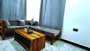 A living room with a sofa, a wooden coffee table, and a small table with a book. - NAHITA APARTMENT (Zanzibar)