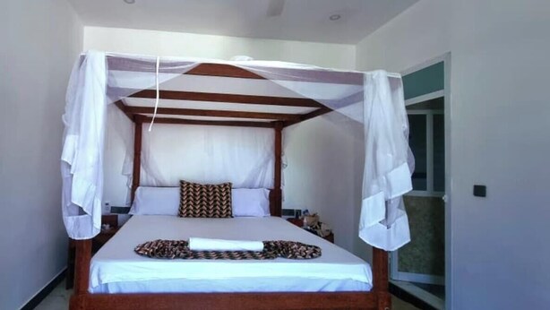 A single bed with a canopy, a bedside table, and a window. - NAHITA APARTMENT (Zanzibar)