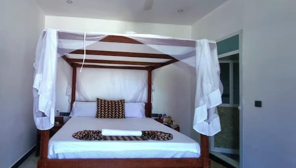A single bed with a canopy, a bedside table, and a window. - NAHITA APARTMENT (Zanzibar)