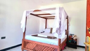 A four-poster bed with a canopy, a bedside table, and a nightstand. - NAHITA APARTMENT (Zanzibar)